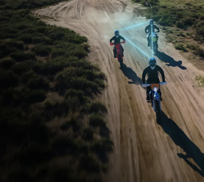 Trzech motocyklistów enduro na piaszczystej drodze połączonych technologią Cardo DMC.